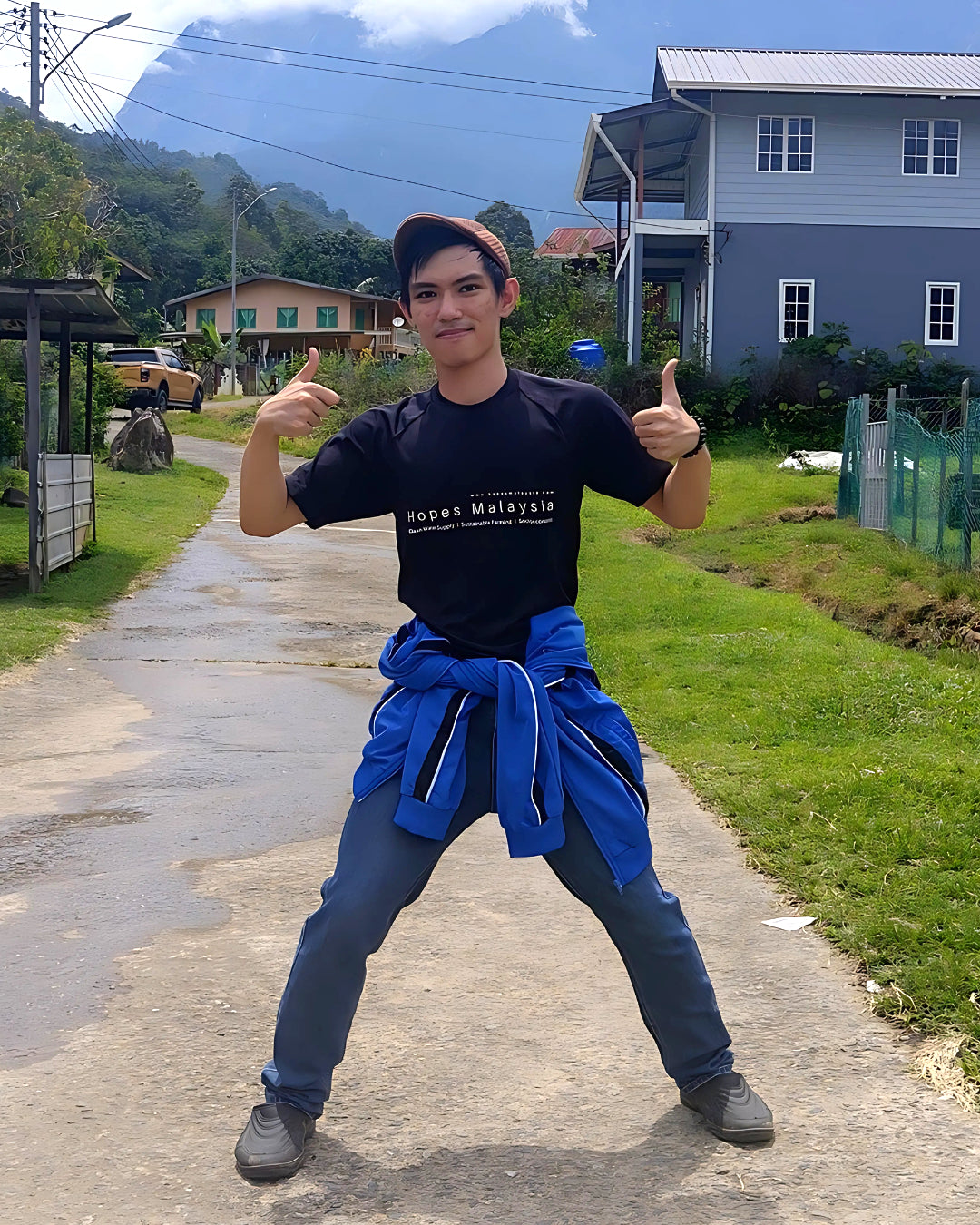 Person in a black shirt giving thumbs up on a rural road.