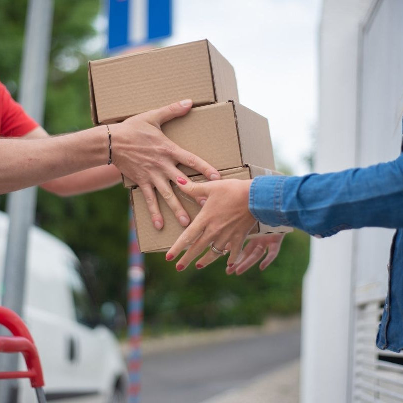 Person receiving a stack of cardboard boxes from another person.