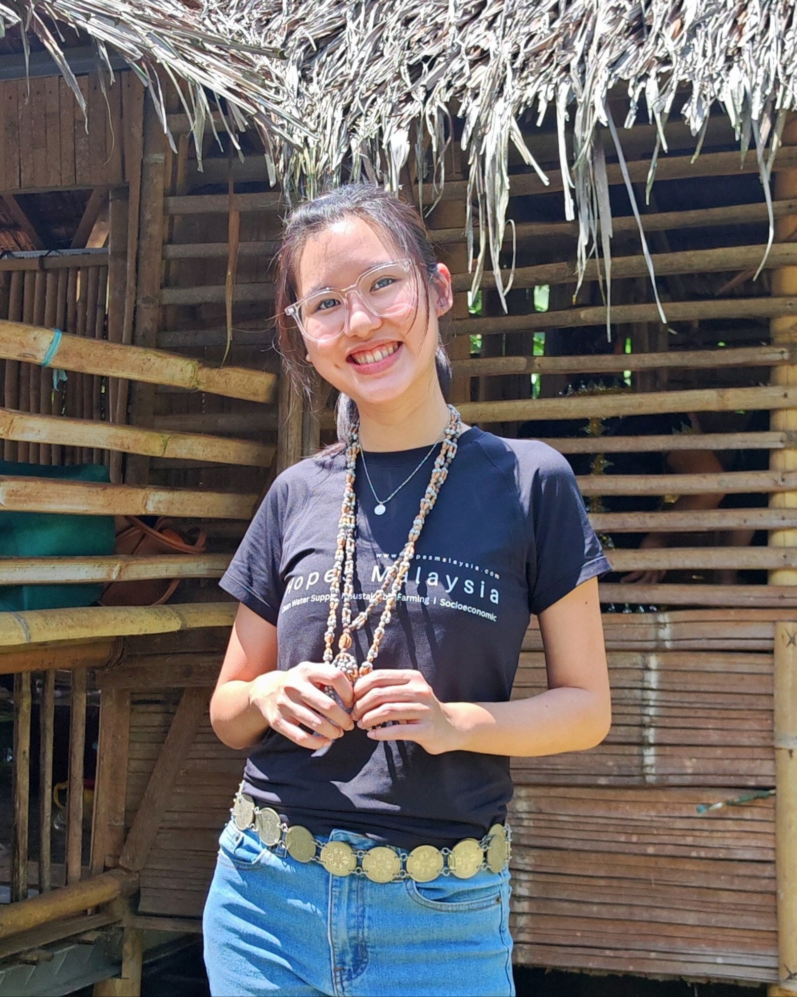 Person wearing a black t-shirt with text and graphics, standing in front of a wooden structure.