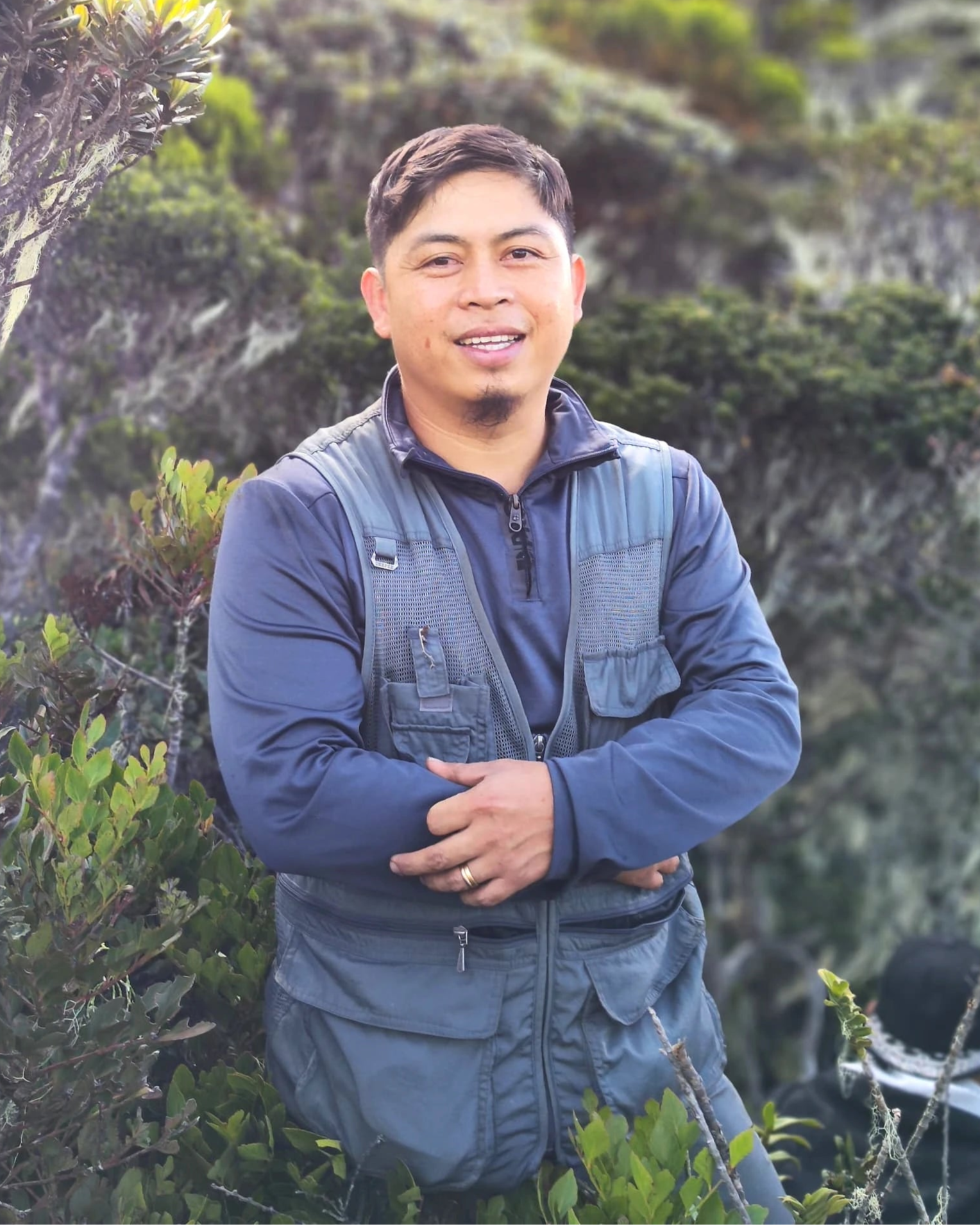 Man standing in a forested area wearing a blue jacket.