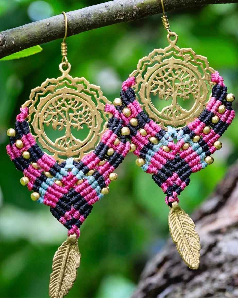 Colorful macrame earrings with gold tree of life design hanging on a branch.