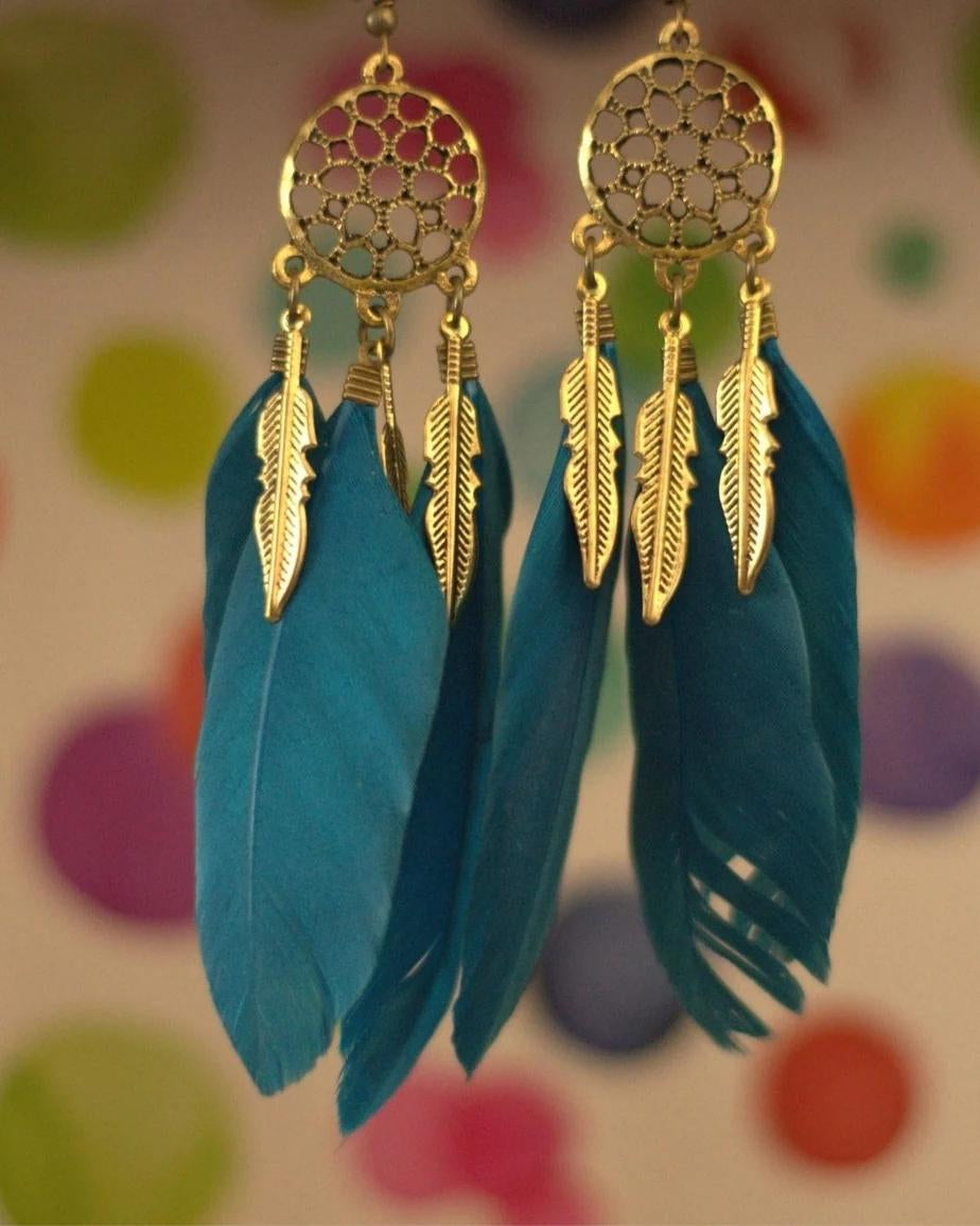 Gold and blue feather earrings on a colorful polka dot background
