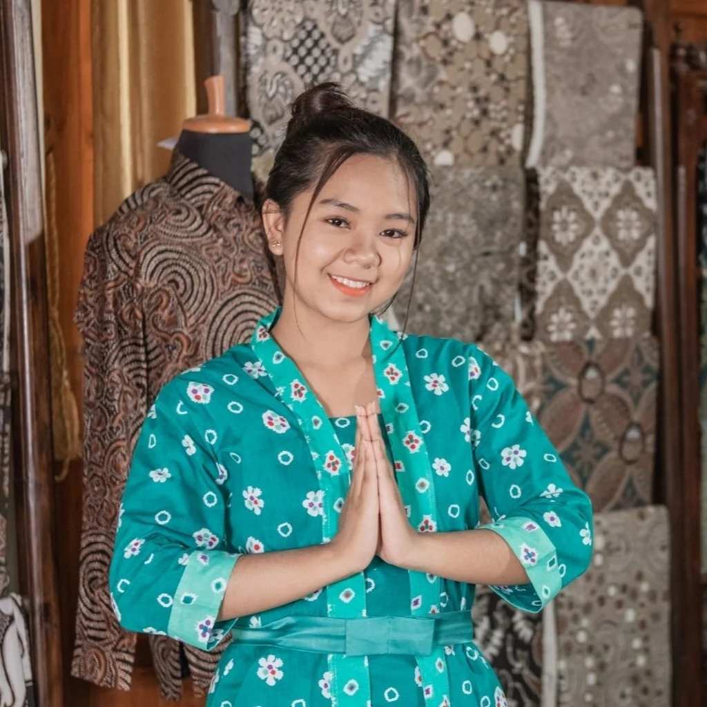 Woman in a teal floral dress standing in front of patterned fabric