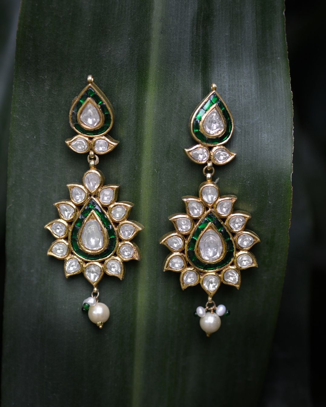 Ornate earrings with green and gold accents on a dark leaf background