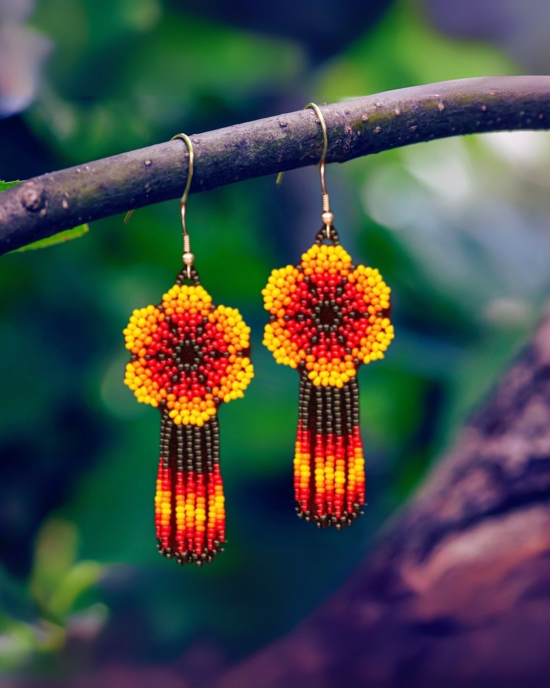 Pair of beaded flower earrings hanging on a branch with a natural background