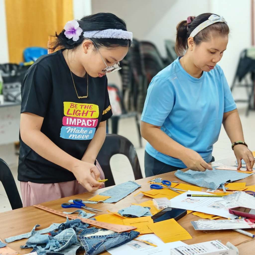 Two women working on a craft project at a table with various materials and tools.
