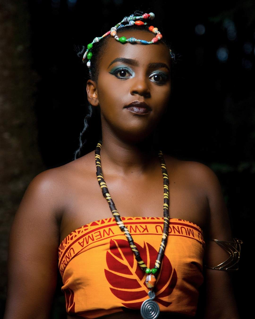 Woman wearing traditional attire with a colorful headpiece and necklace against a dark background