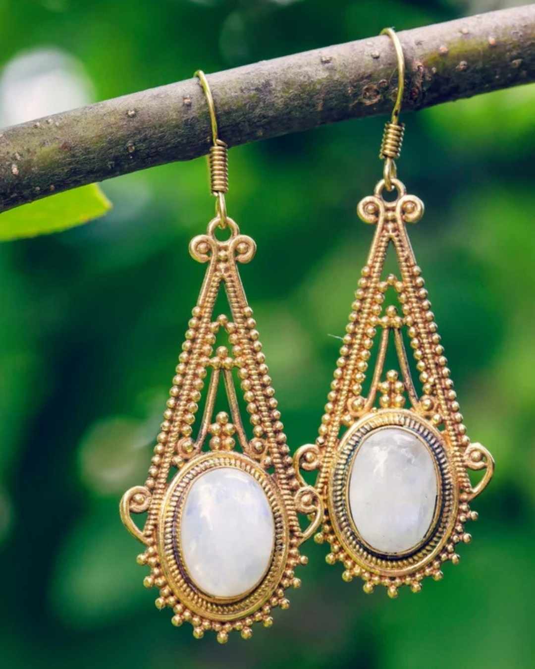 Gold earrings with white stones on a branch against a green leafy background