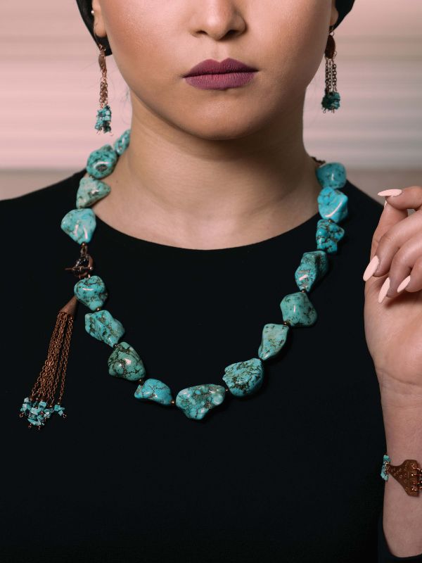 Turquoise necklace and earrings on a person against a neutral background