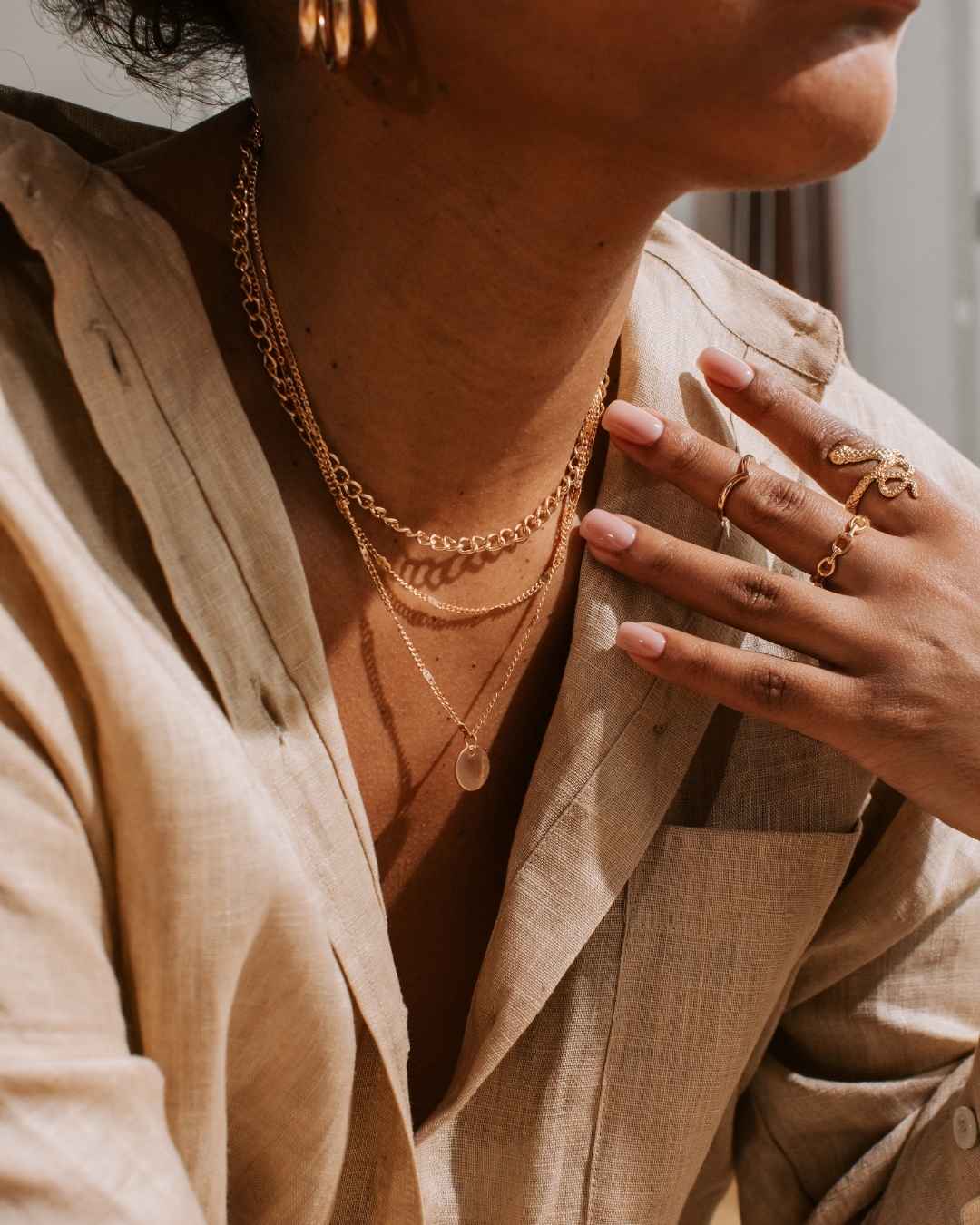 Close-up of a person wearing gold jewelry including necklaces and rings.