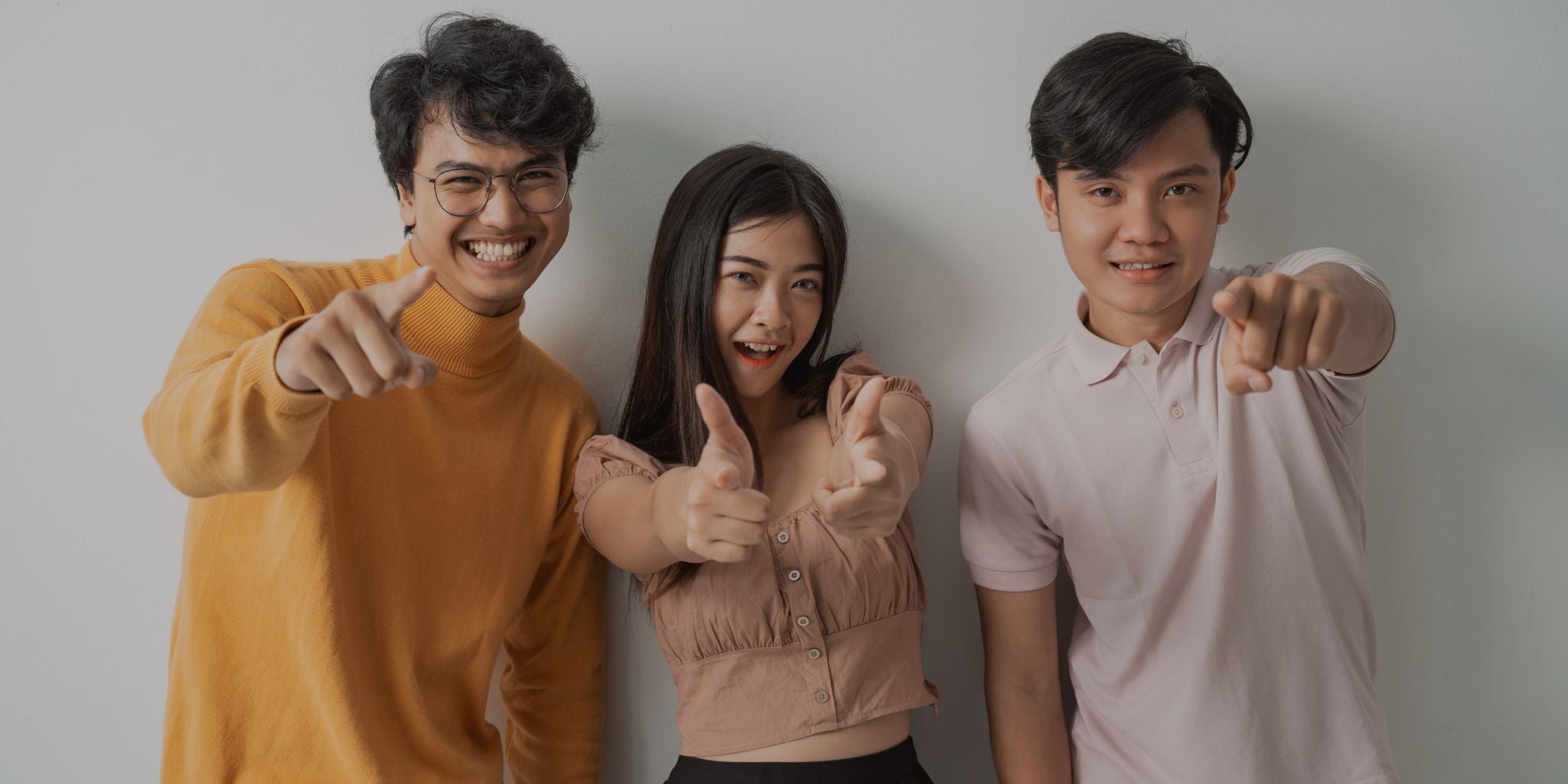 Three people posing together with thumbs up against a plain background