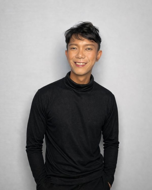 In house designer, Asraf, in a black high neck outfit, standing in front of a plain white background