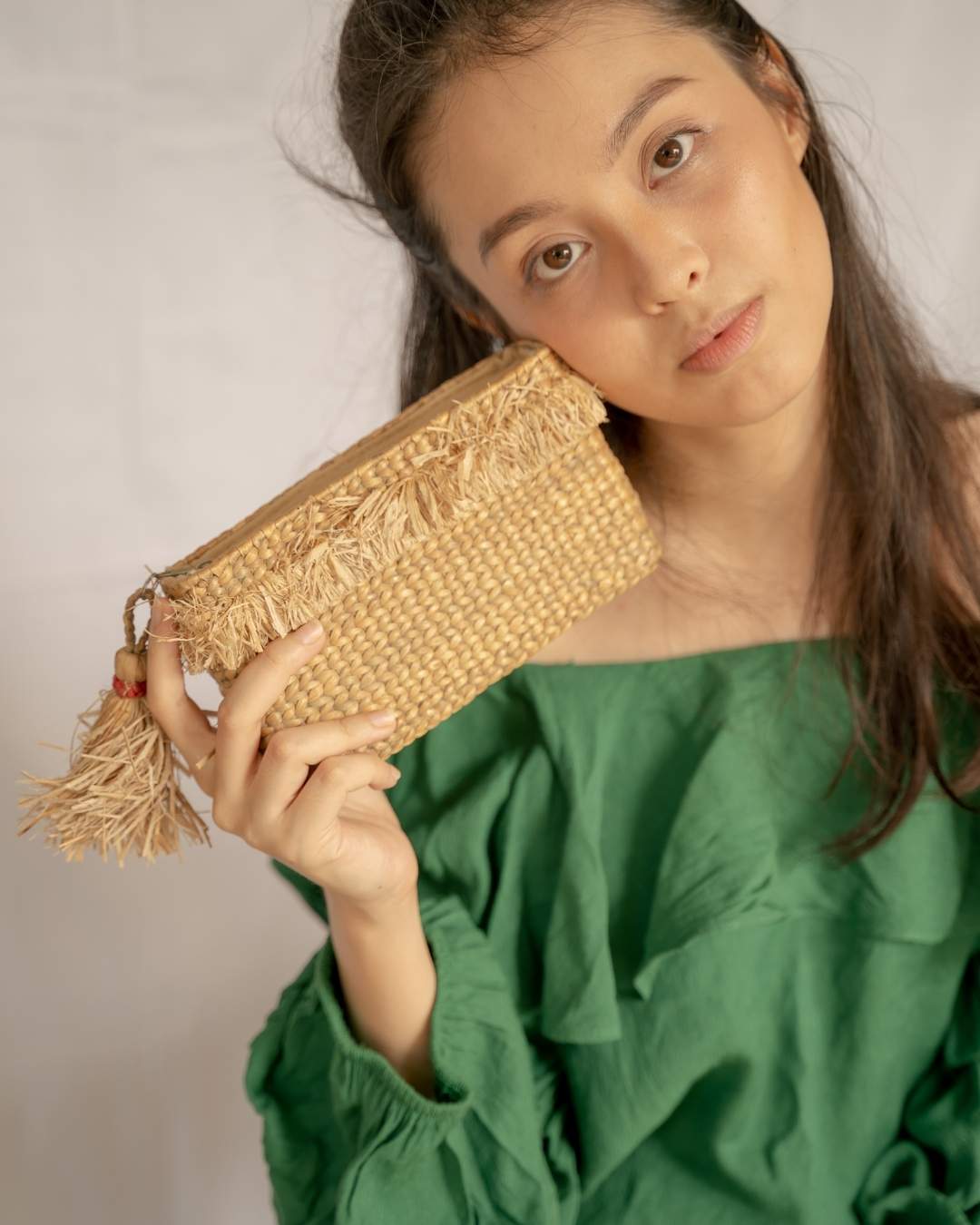 Woman holding a woven clutch bag against a plain background