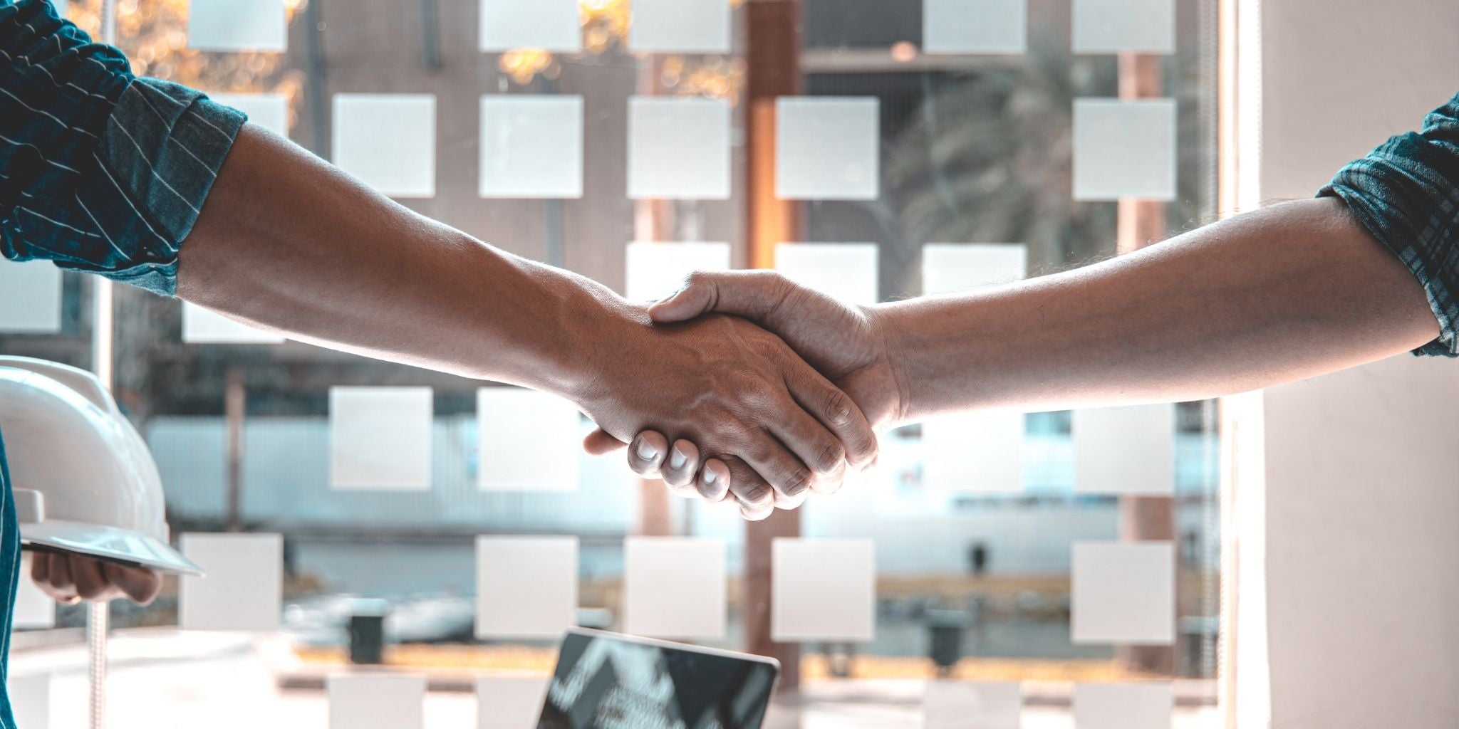 Two people shaking hands in an office setting, signifying collaboration between two parties