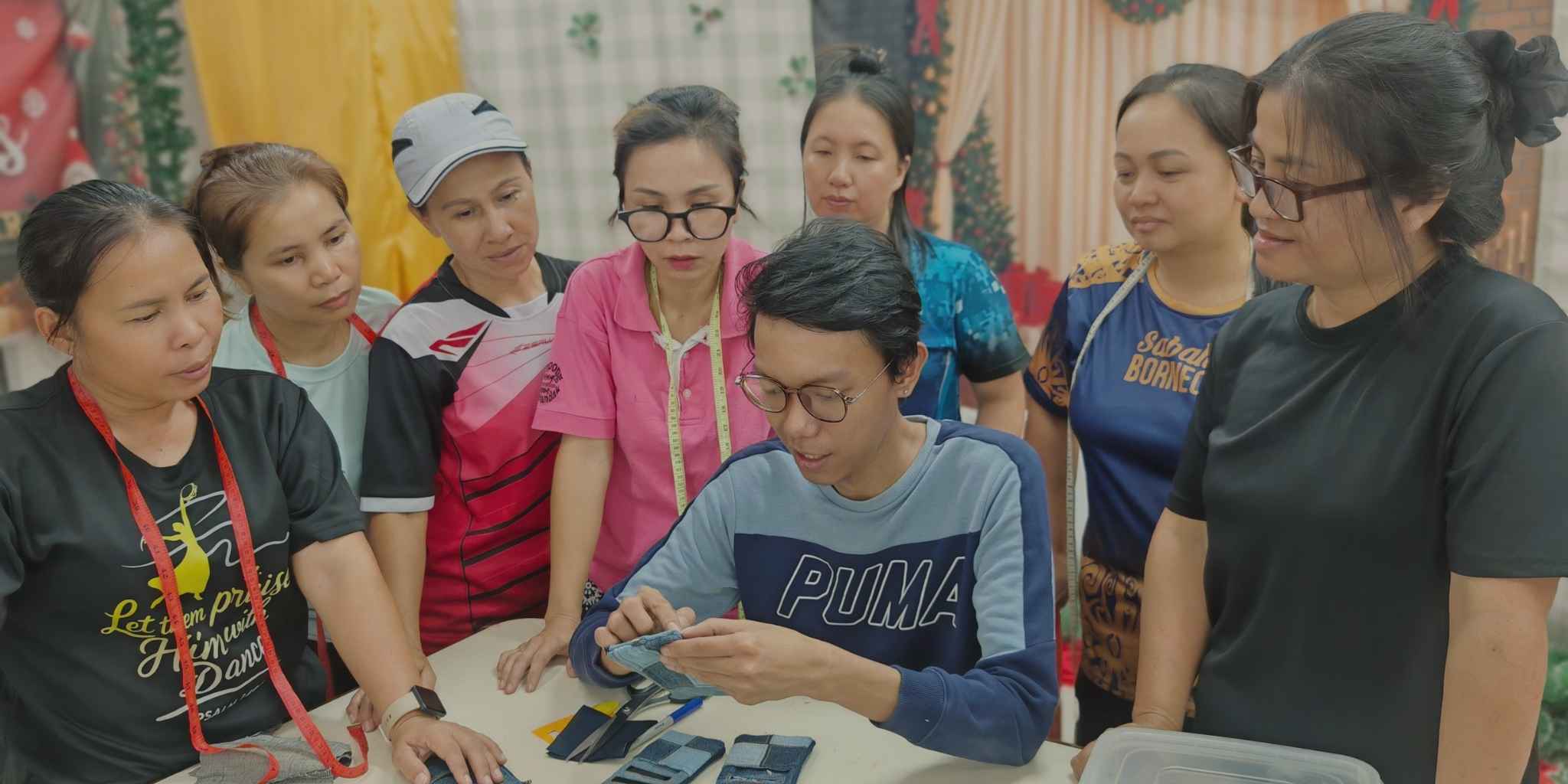 Group of rural women gathered around a table with designer showing proper methods to sew neatly