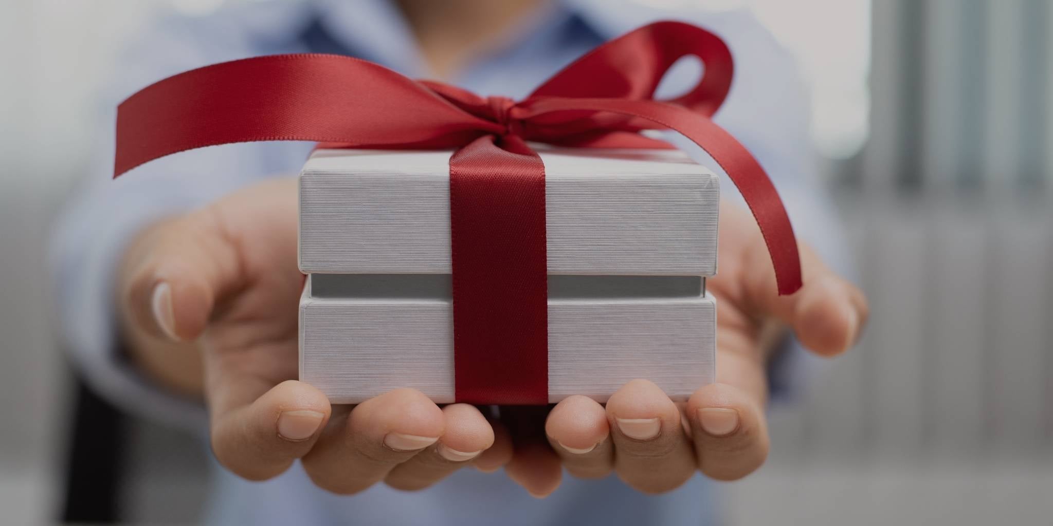 Person holding a white gift box with a red ribbon