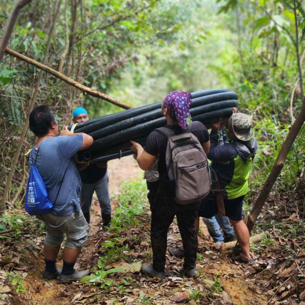 Group of rural villagers carrying a roll of water pipelines into the project area for gravity water project
