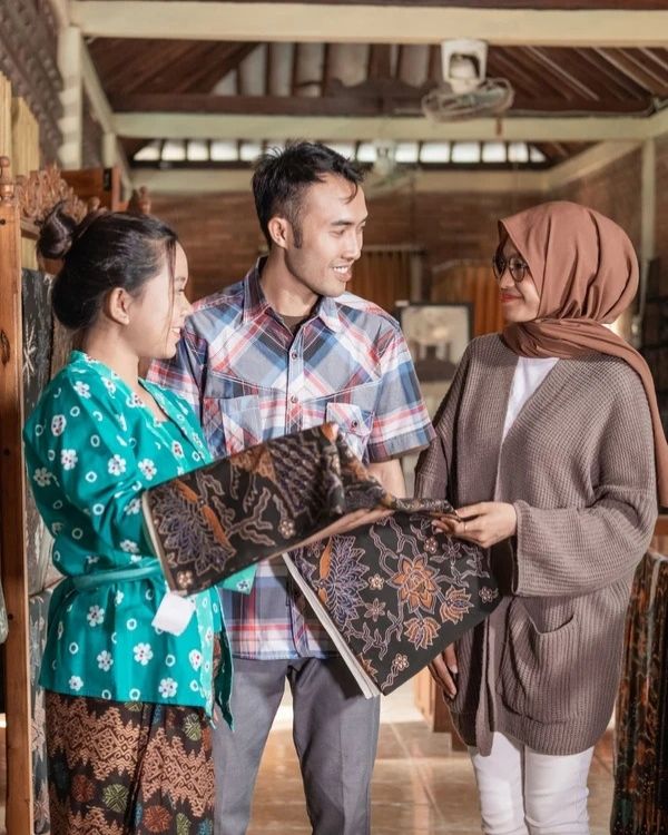 Three people looking at a batik fabric in a traditional setting