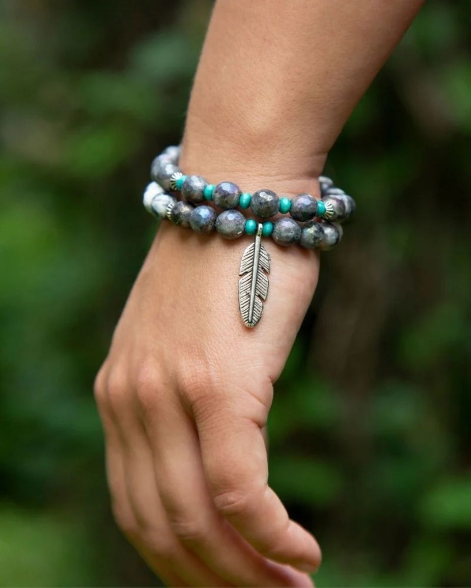 Hand wearing a bracelet with a feather charm against a blurred green background