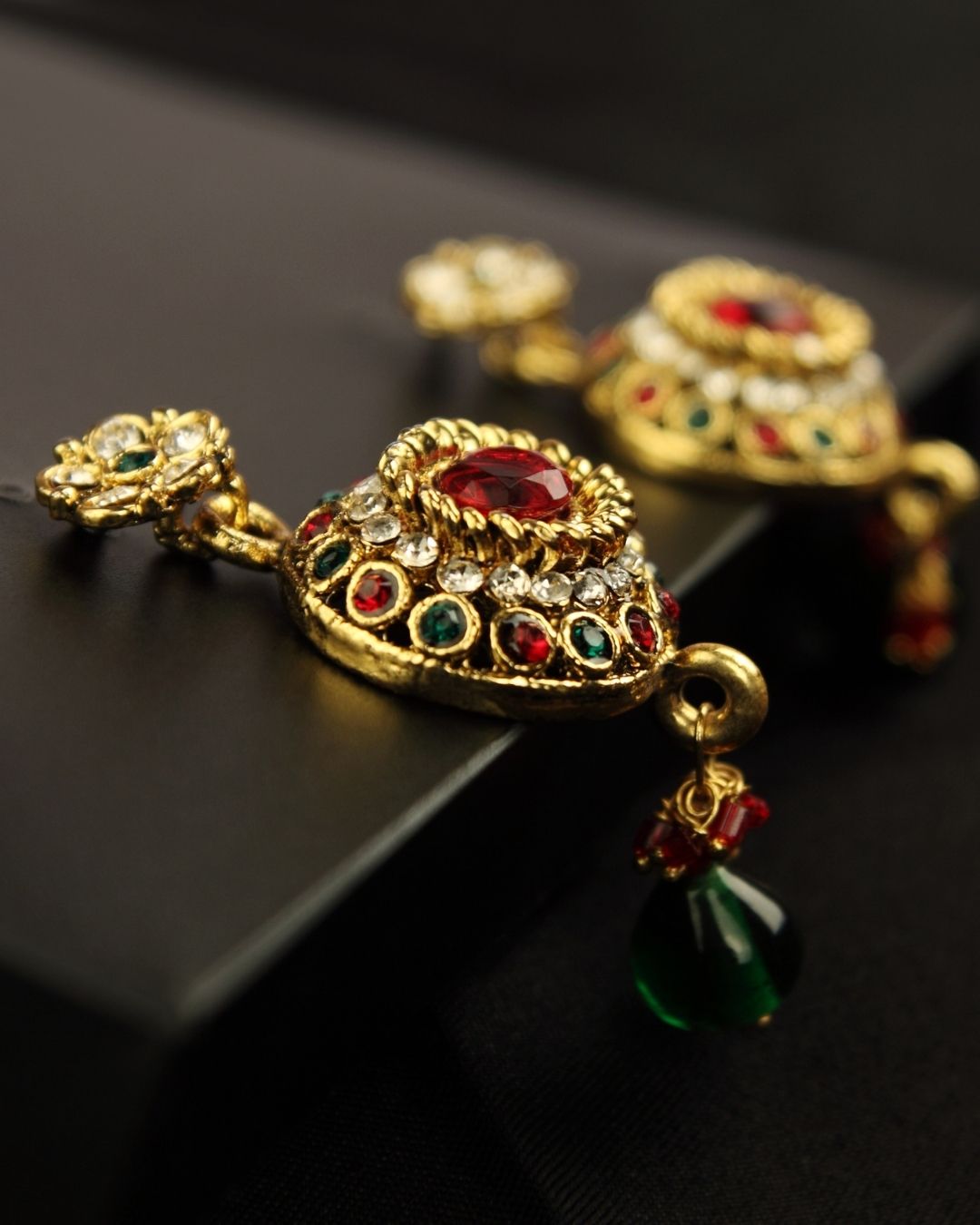 Ornate gold earring with gemstones on a black surface