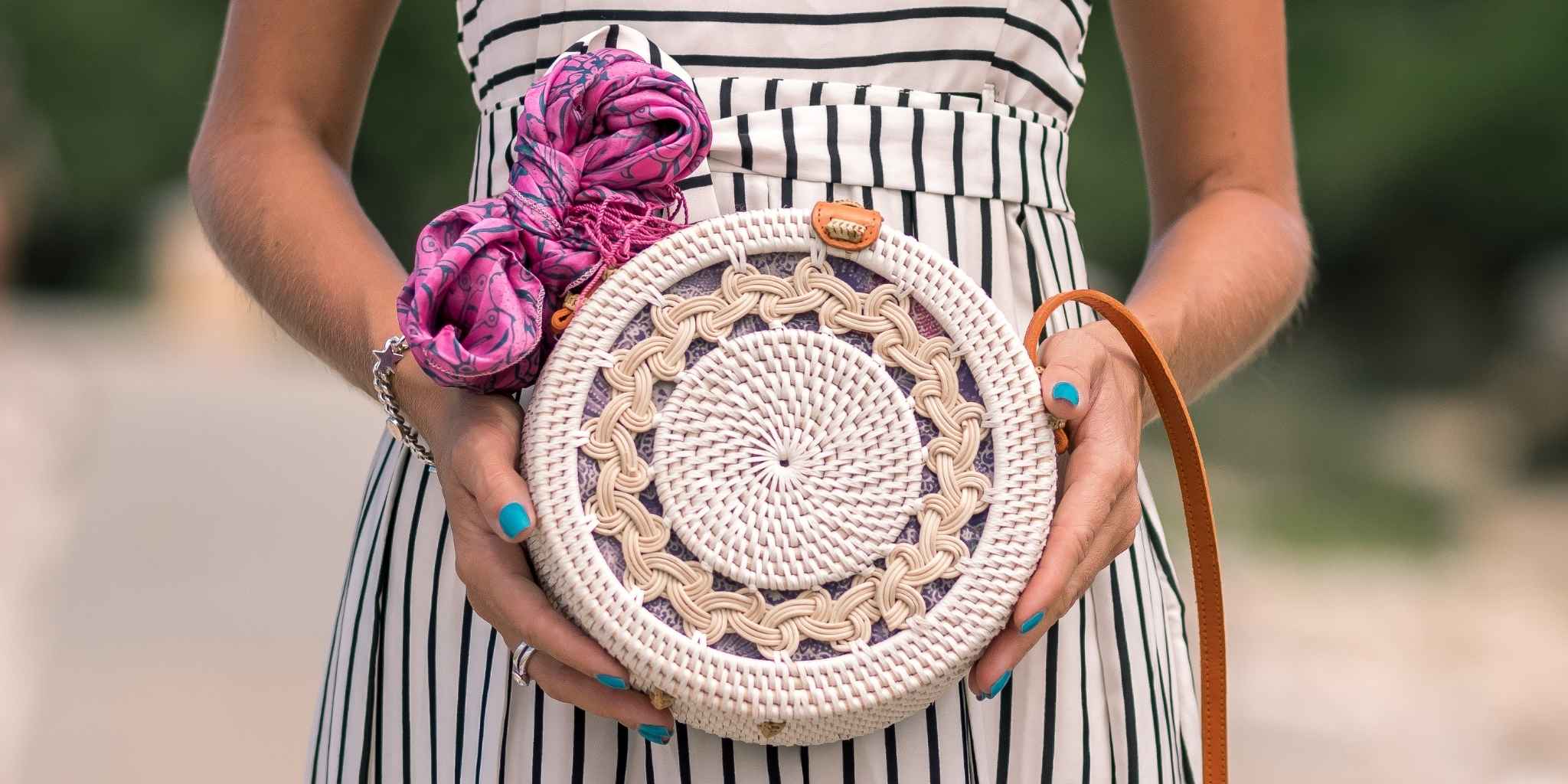 Person holding a round woven bag with a decorative pink top, blurred background