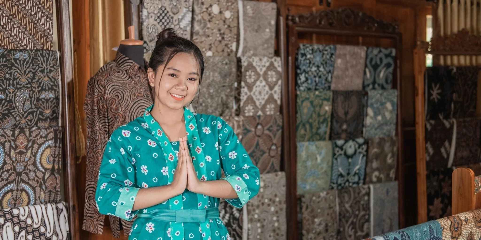 Woman in a teal floral dress standing in front of a wall of patterned textiles.