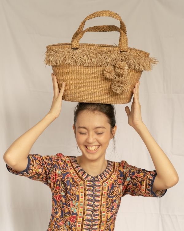Woman holding a woven basket on her head against a plain background