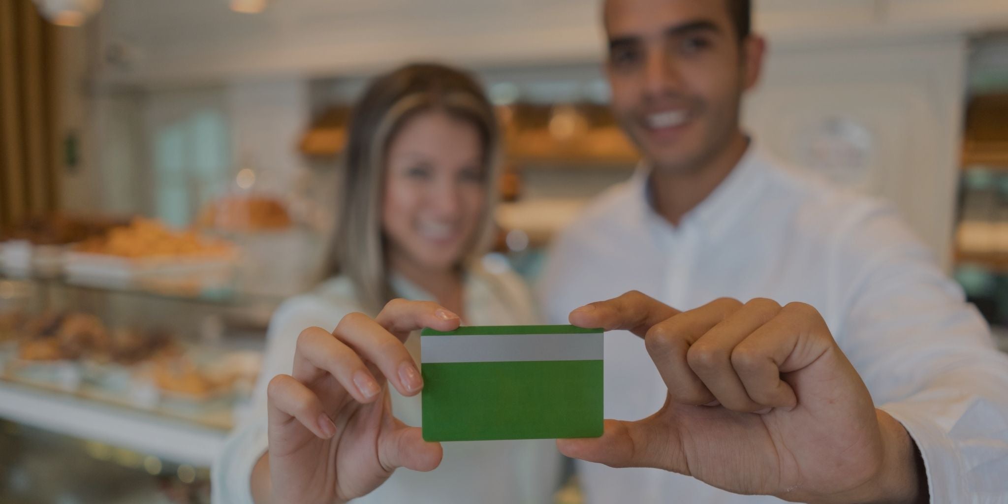 Two people holding a green credit card in a blurred indoor setting