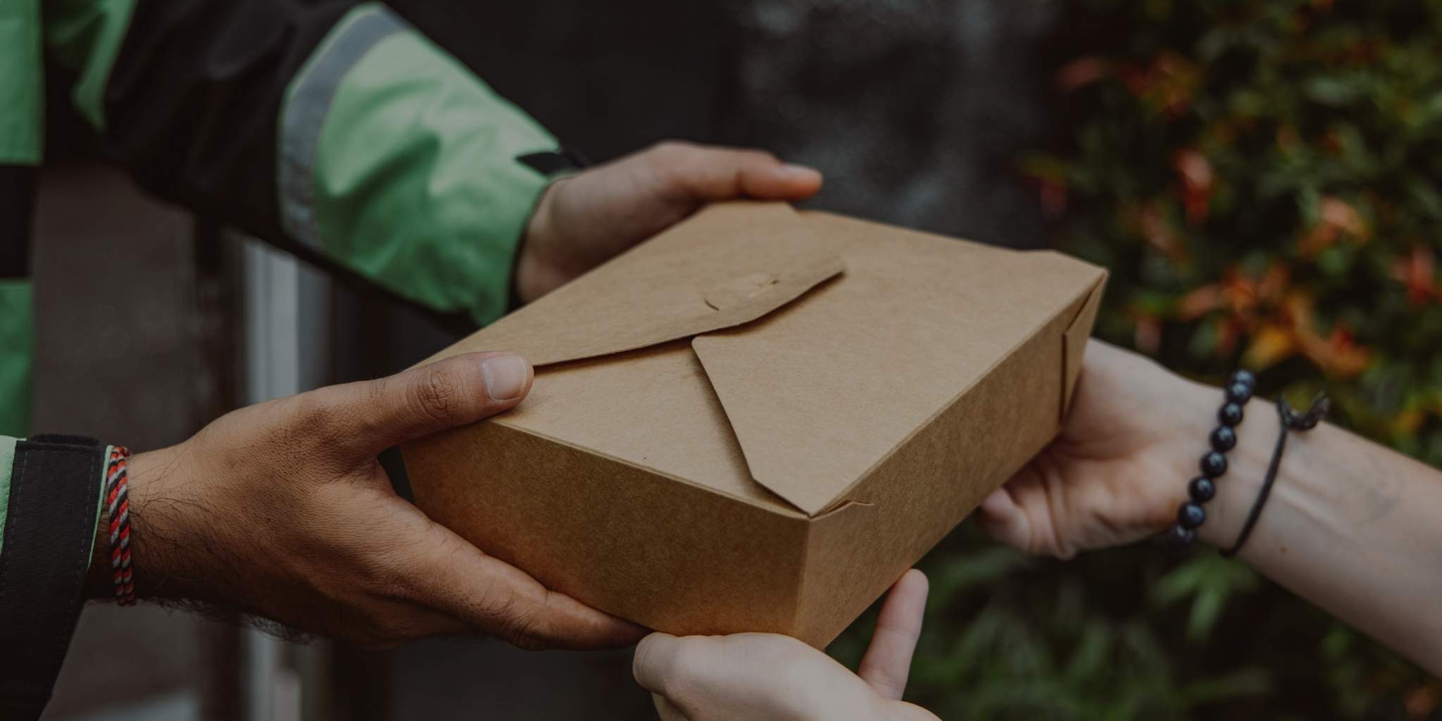Two people exchanging a brown package outdoors.