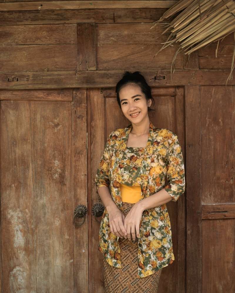 Woman in a floral kebaya outfit standing in front of a wooden door
