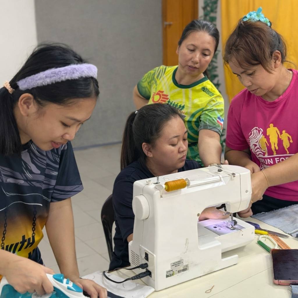 Group of rural women learning to use a sewing machine in a classroom setting.
