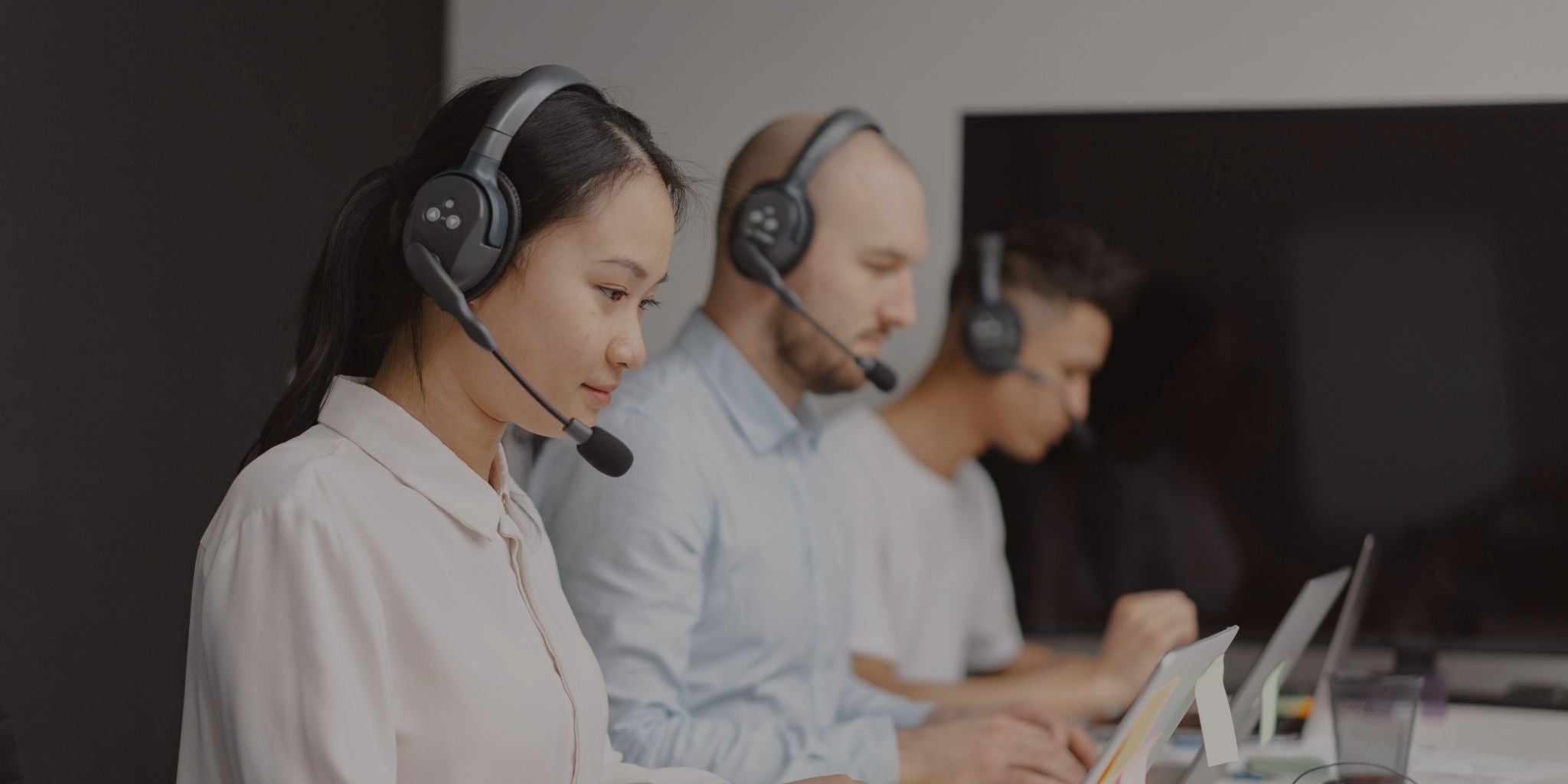 Three call center agents wearing headsets and working on computers.