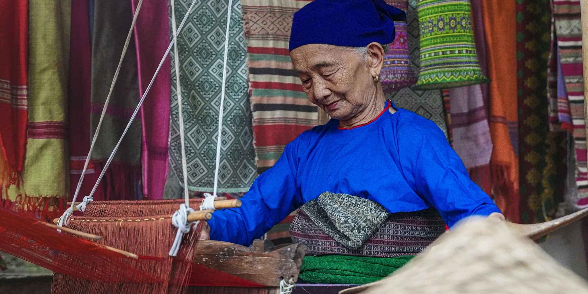 Elderly woman weaving with a traditional loom in a colorful setting