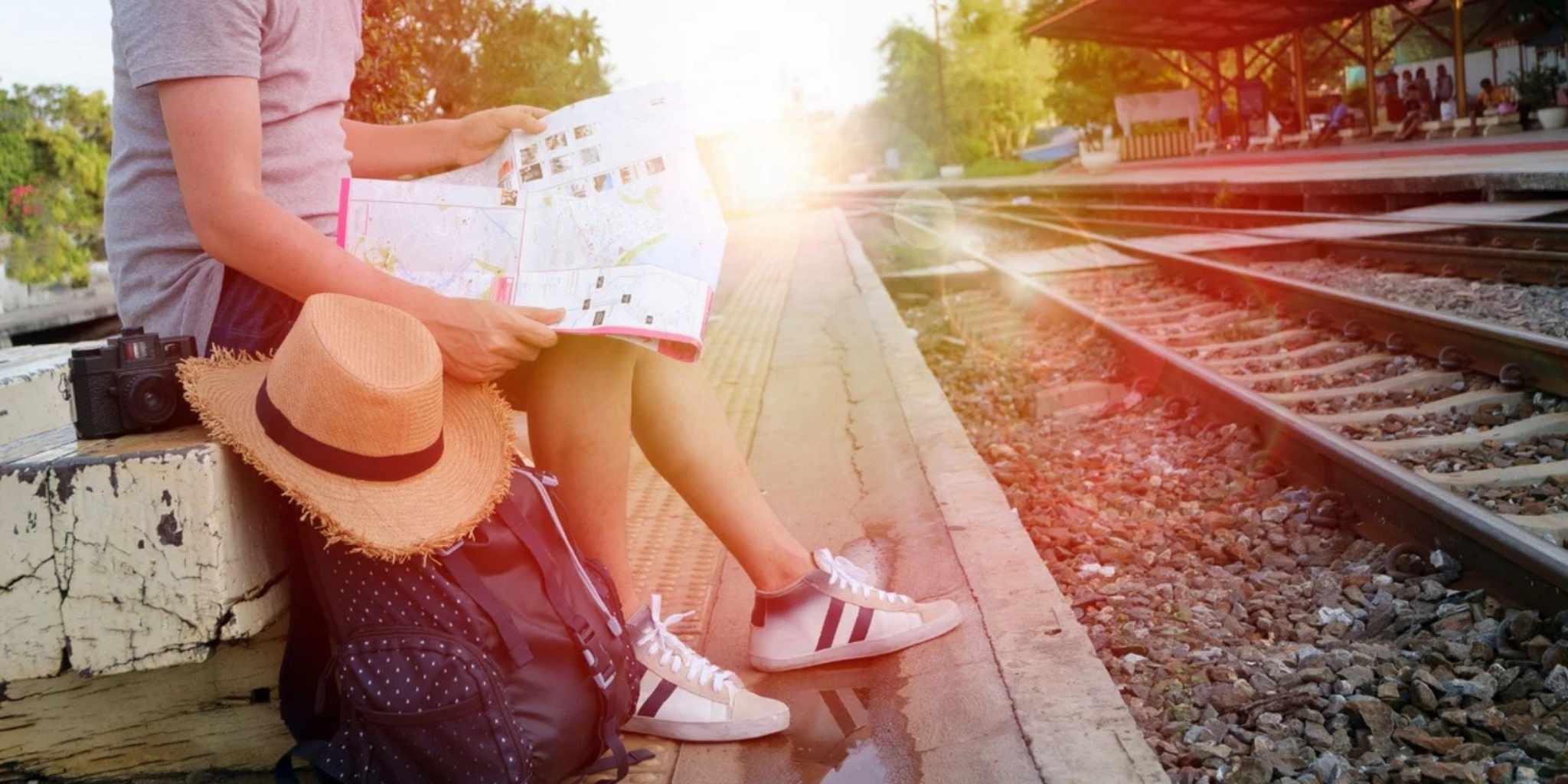 Person sitting on a train platform with a map, wearing a hat and shoes, with a scenic background.