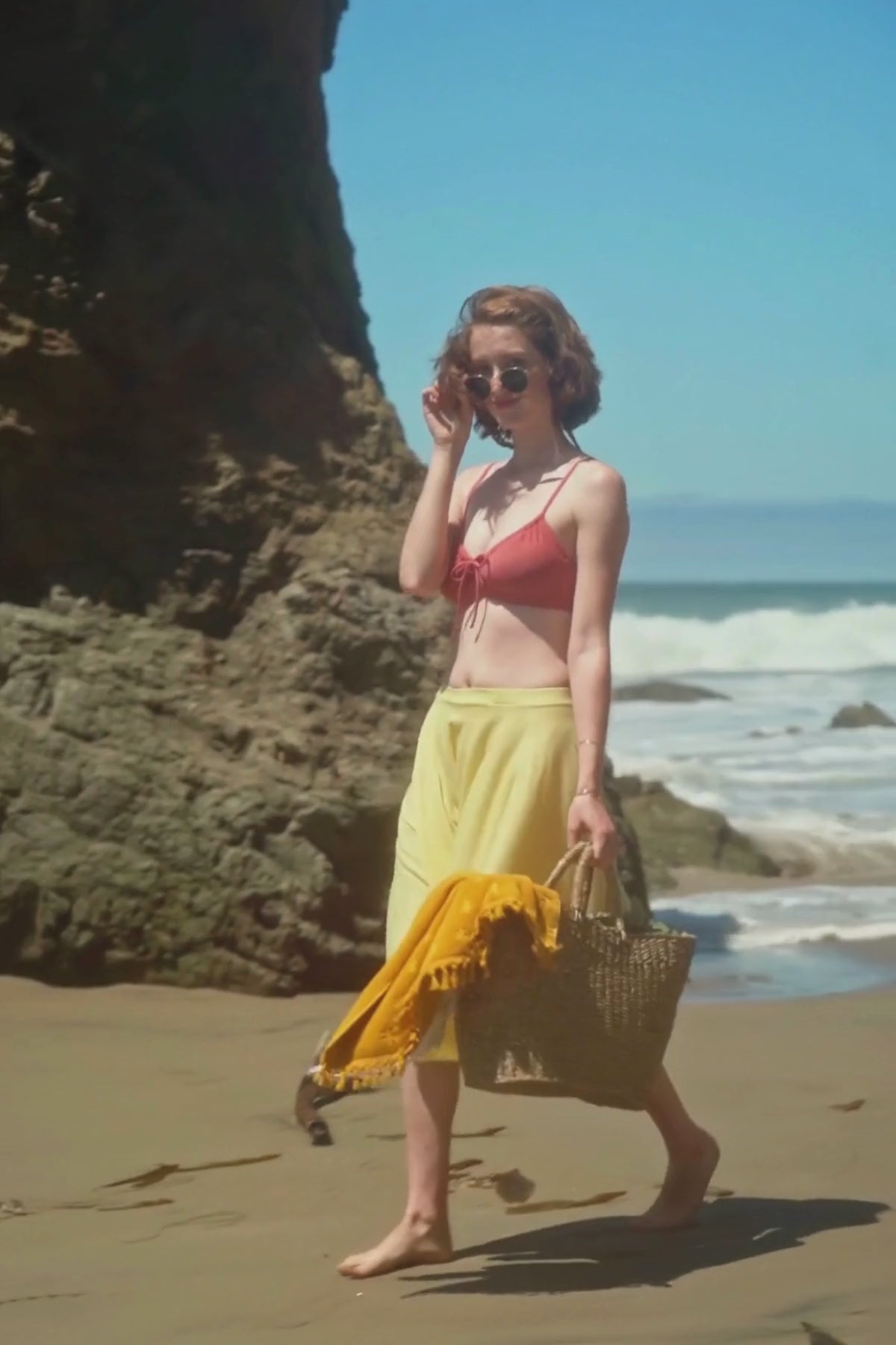 woman walking along the beach while carrying a rattan bag