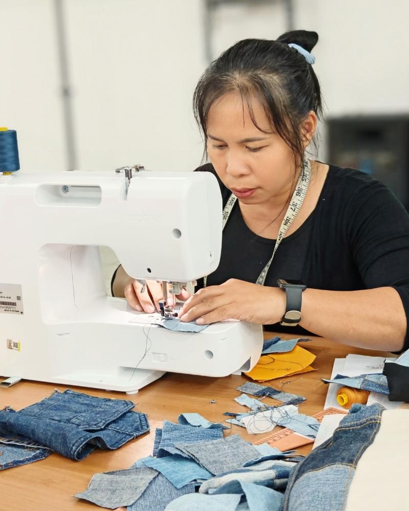 A rural woman working on a sewing machine with fabric pieces around
