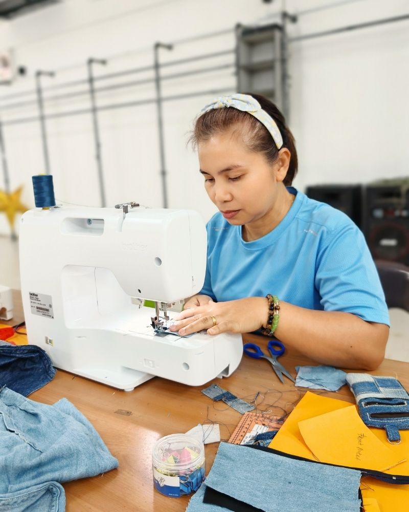 A rural woman working on a sewing machine with fabric and tools around
