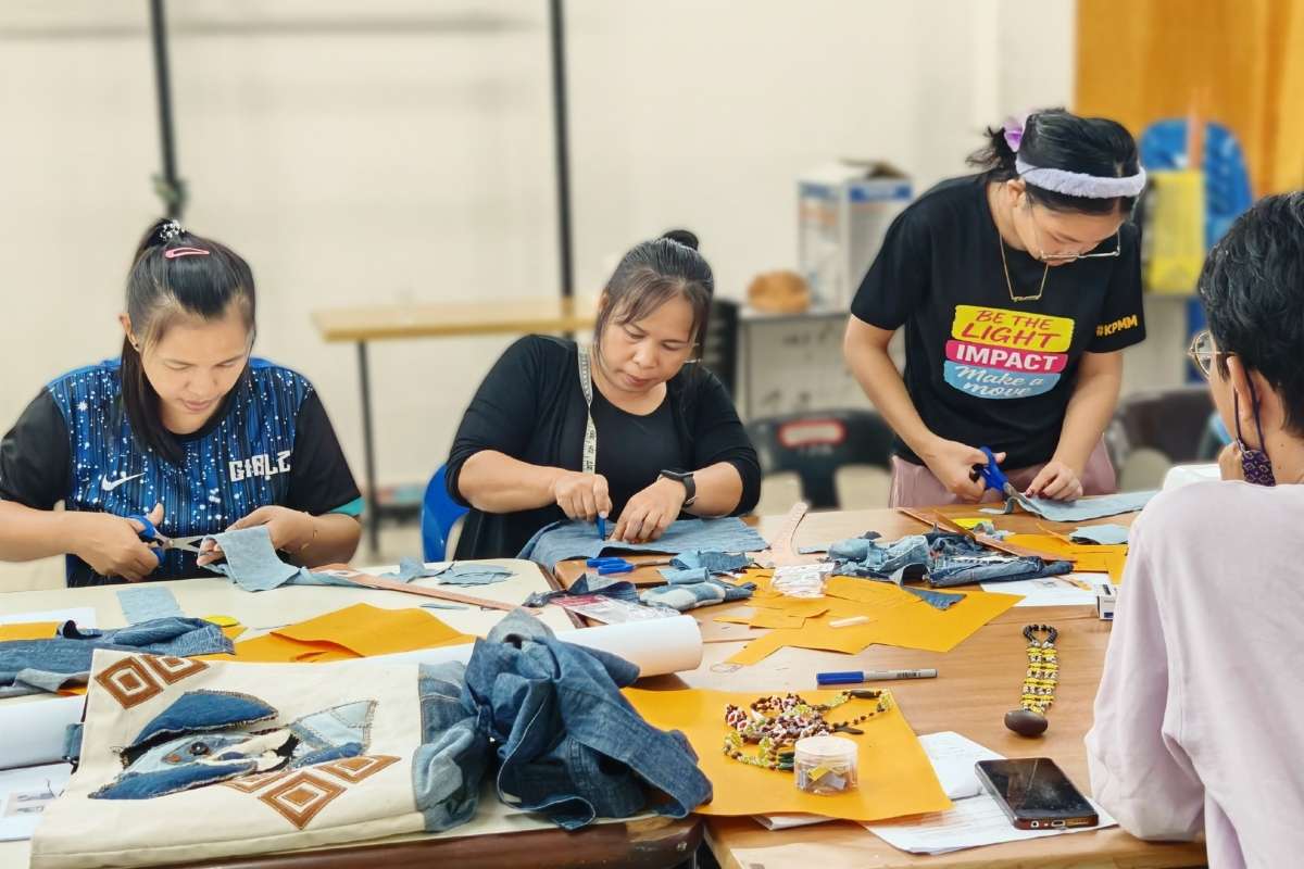 Four people working on sewing projects at a table with upcycled fabric and tools.